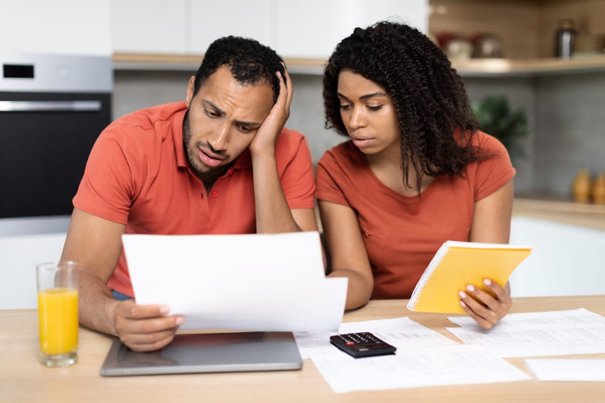 Despaired millennial black family in red t-shirts work with documents, check bills, have problems with calculate bookkeeping in kitchen interior. Stress, crisis at home, debts, credit and mortgage